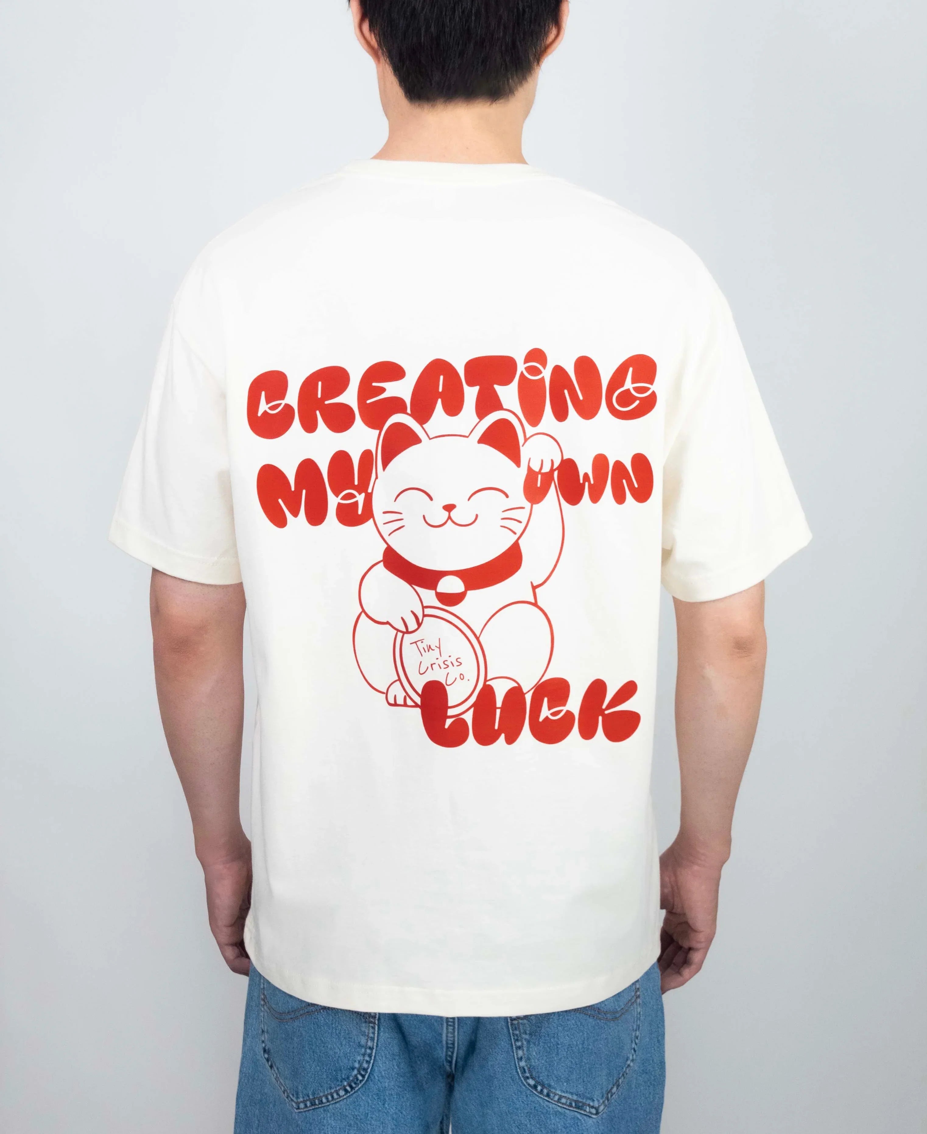 Person wearing a white t-shirt with red text and a graphic of a cat on the back, standing against a plain background.