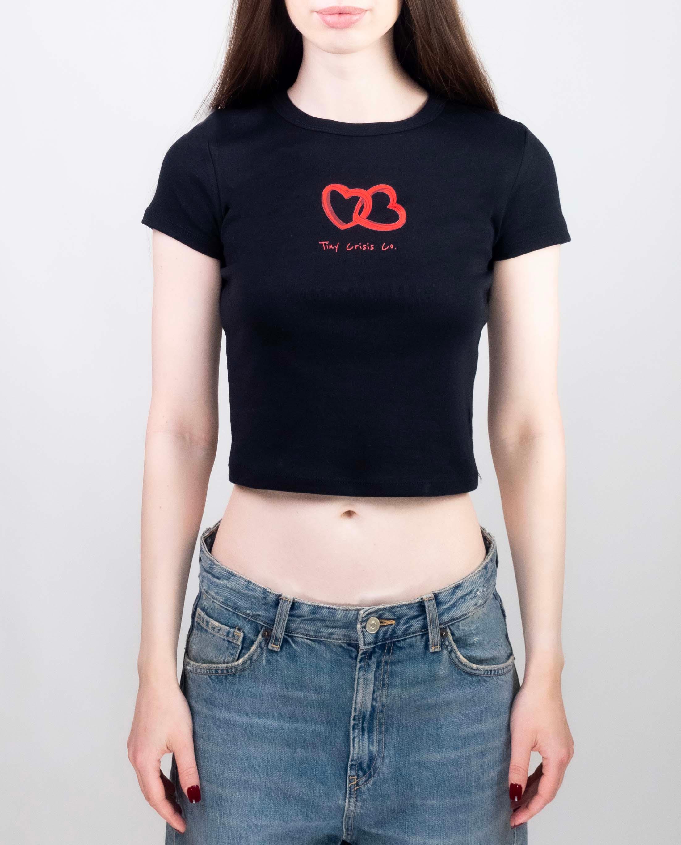 Person wearing a black crop top with a red logo and blue jeans on a plain background