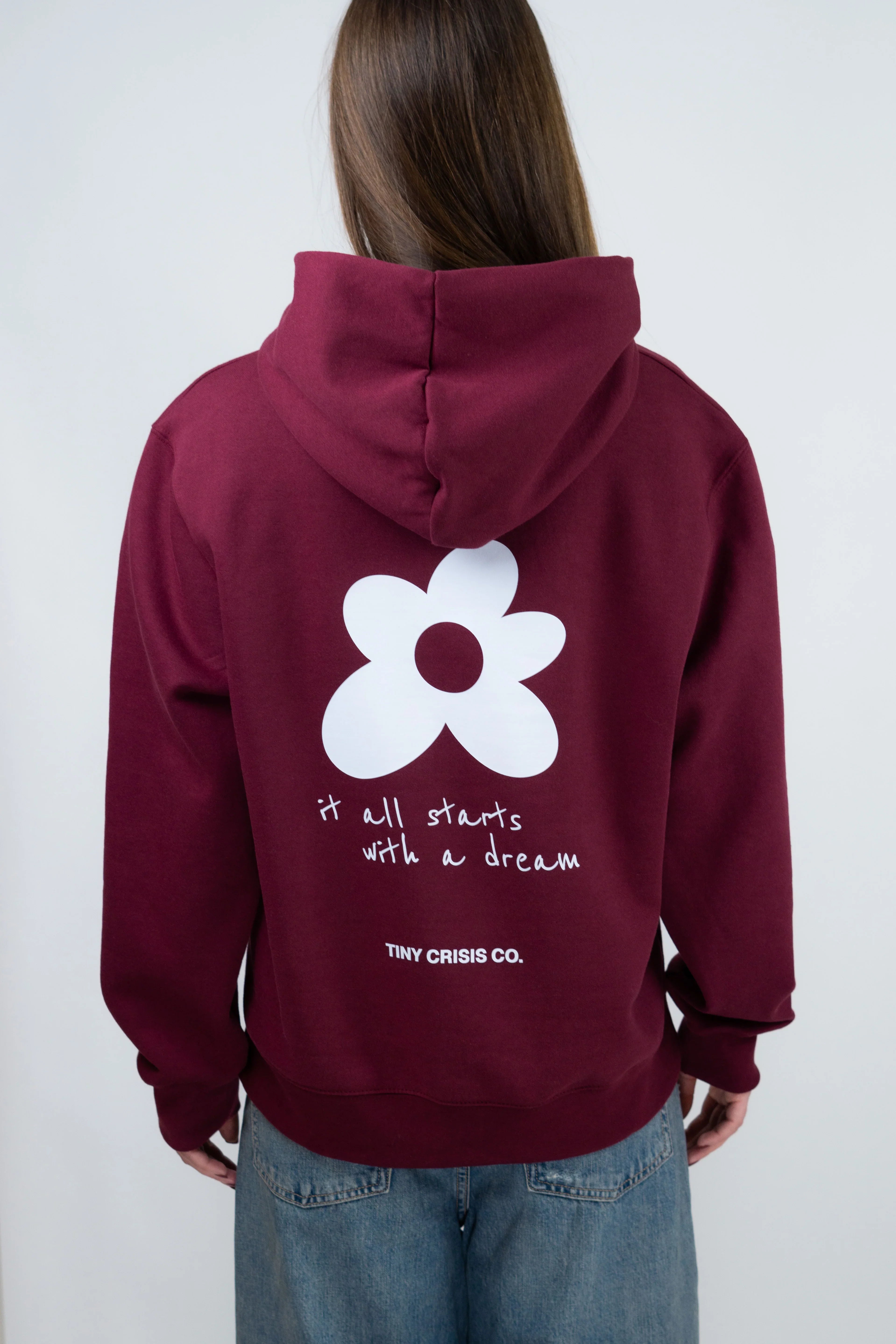 Person wearing a maroon hoodie with a white flower design and text on the back, on a plain background.