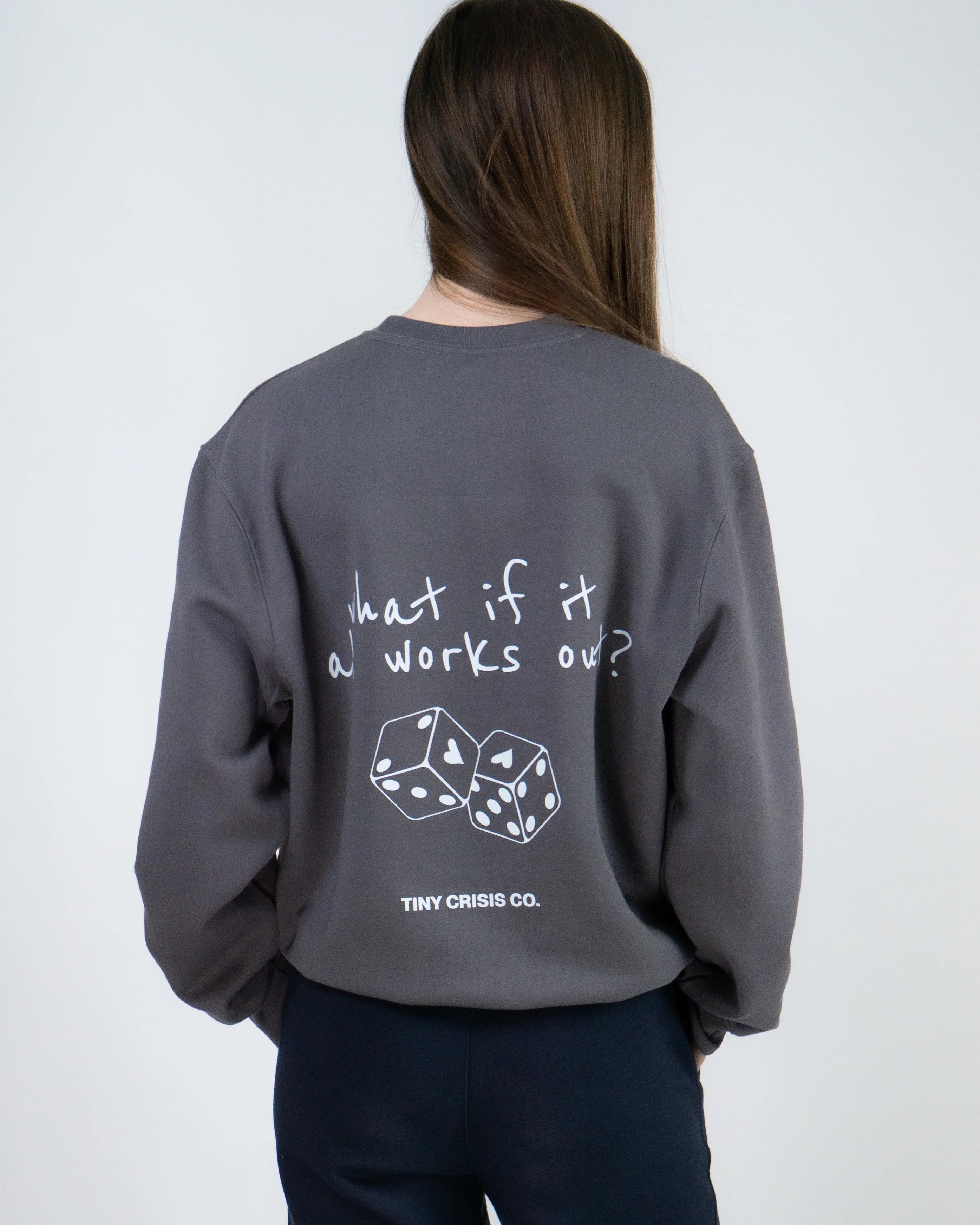 Person wearing a gray sweatshirt with text and dice design on the back, on a plain background